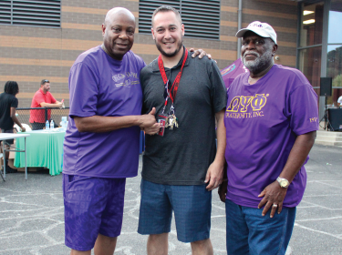 three man standing side by side wearing purple shirts
